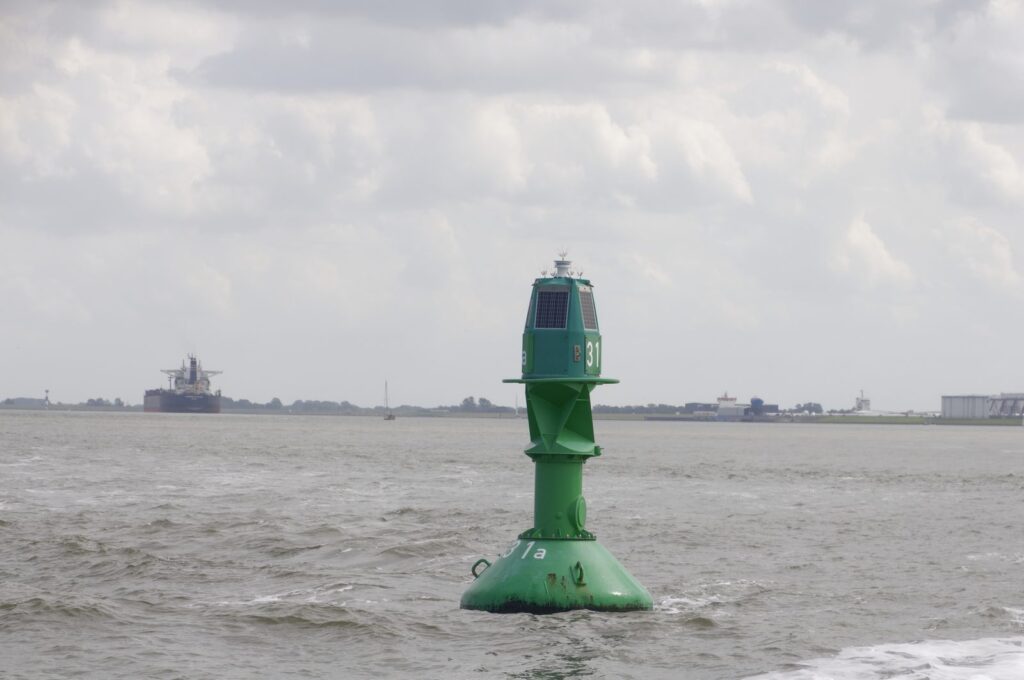 Grüne Fahrwassertonne in der Elbe vor Cuxhaven, dahinter ein Frachtschiff