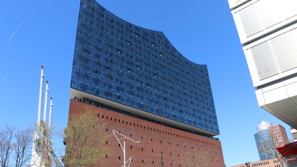Geschwungene Glasfassade der Elbphilharmonie über dem Backsteinsockel vor blauem Himmel