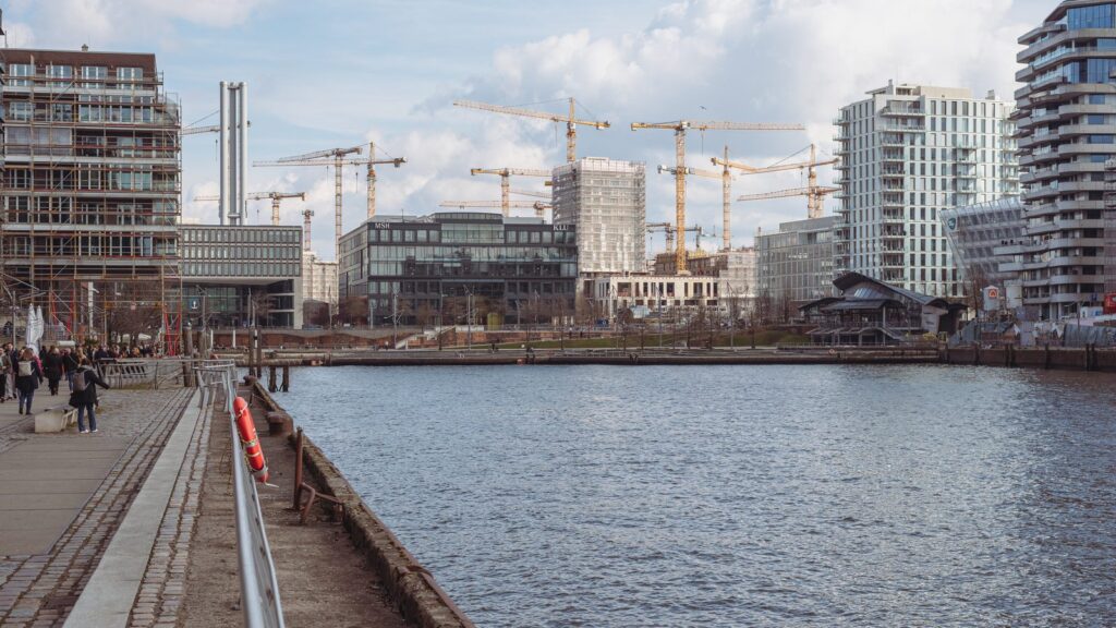 Blick über ein Hafenbecken der HafenCity auf moderne Neubauten und Baukräne
