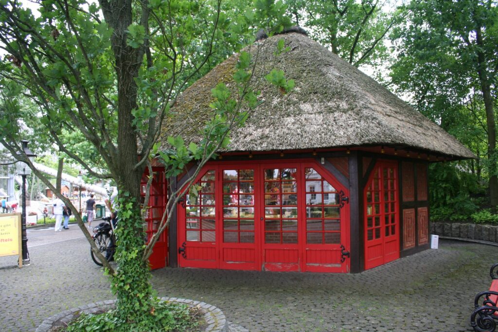 Roter Verkaufspavillon mit Reetdach unter alten Bäumen im Heide Park
