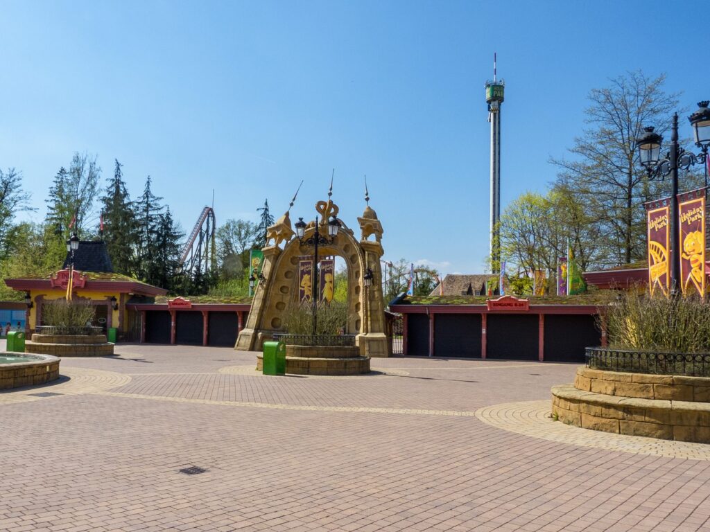 Eingangsplatz mit Freifallturm und Achterbahn über den Baumwipfeln im Frühling