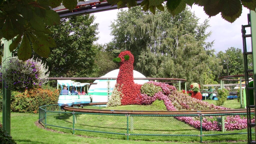 Blumenfigur eines Pfaus in der Parkanlage, dahinter fährt eine Parkbahn vorbei