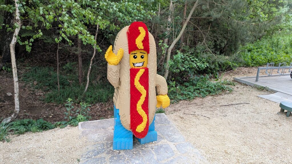 Übergroße Lego-Figur im Hotdog-Kostüm an einem Waldweg im Legoland