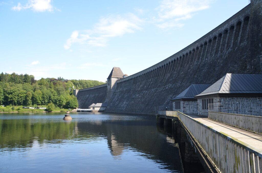 Staumauer der Möhnetalsperre im Sommer mit Uferweg und Spiegelung im Ausgleichsweiher