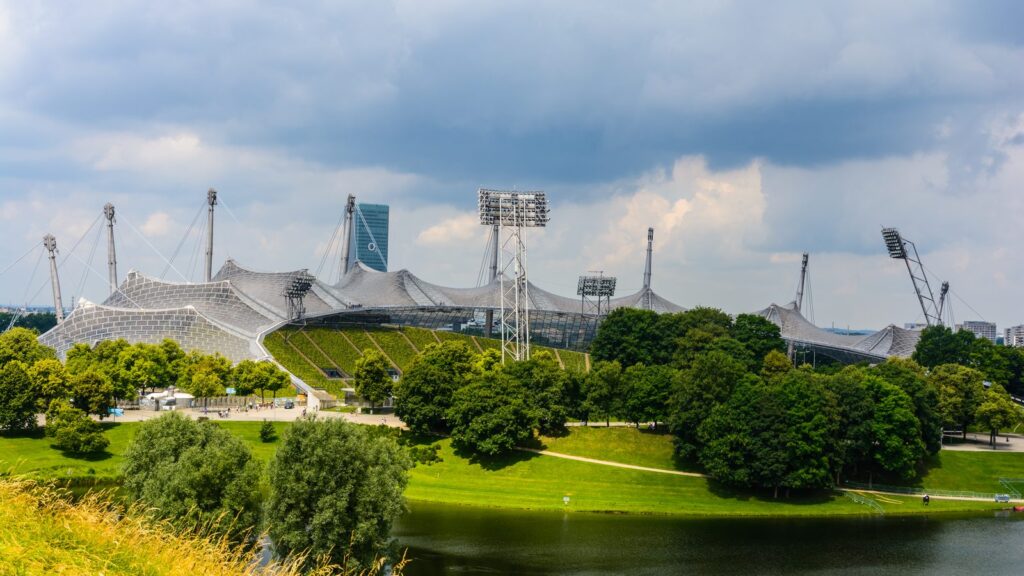 Olympiastadion München mit Zeltdach und Olympiasee unter sommerlichem Wolkenhimmel