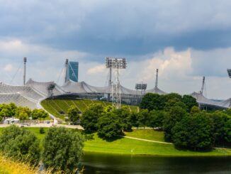 Olympiastadion München mit Zeltdach und Olympiasee unter sommerlichem Wolkenhimmel
