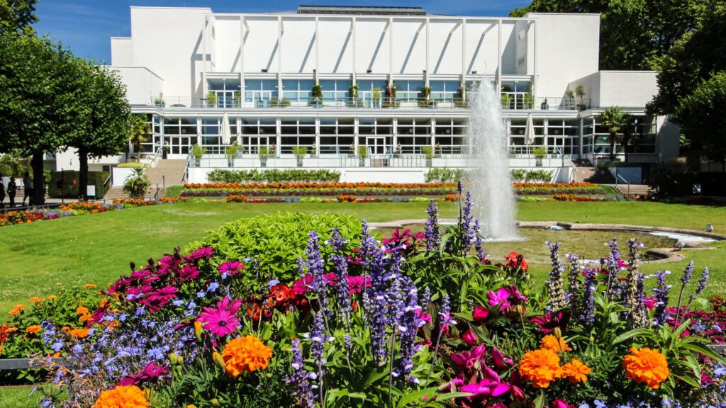 Gesellschaftshaus im Palmengarten mit Springbrunnen und bunten Blumenbeeten im Sommer