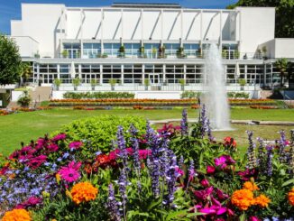 Gesellschaftshaus im Palmengarten mit Springbrunnen und bunten Blumenbeeten im Sommer