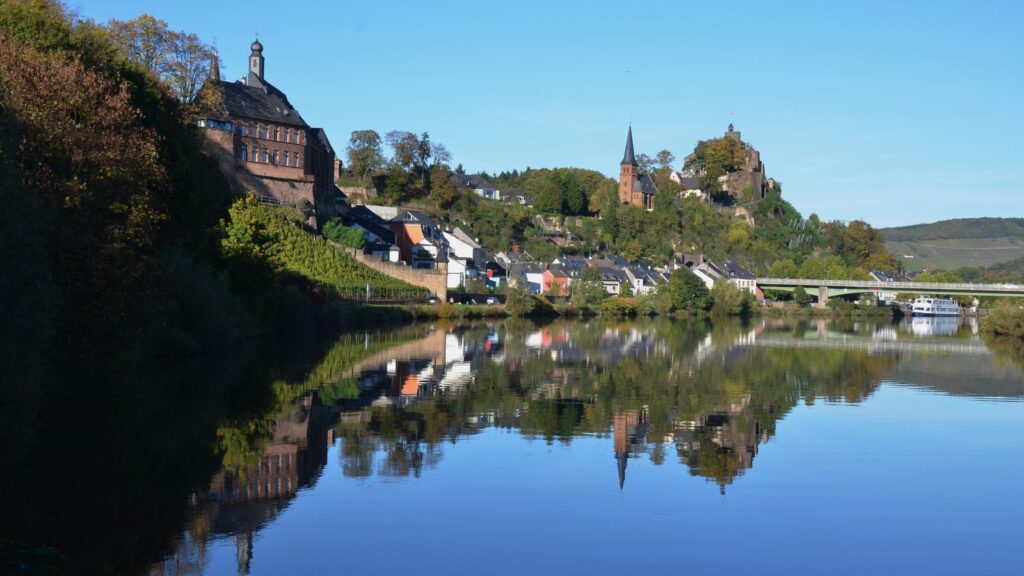 Saarburg mit Burgruine und Kirchturm spiegelt sich im Herbst in der Saar