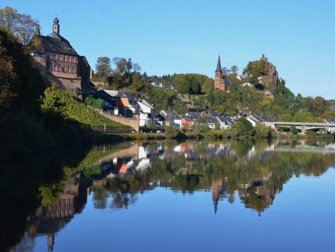 Saarburg mit Burgruine und Kirchturm spiegelt sich im Herbst in der Saar