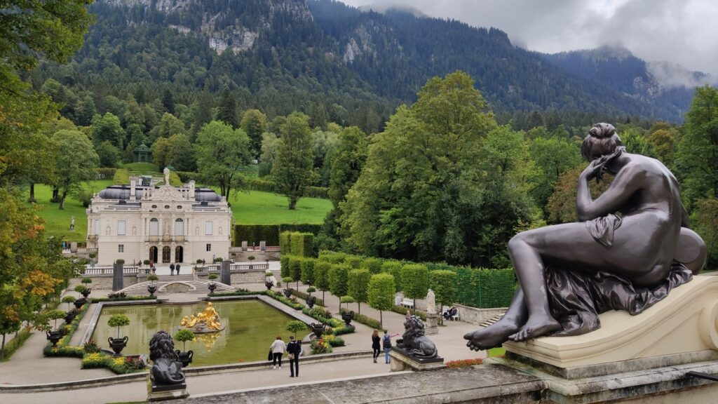 Wasserparterre mit vergoldeter Fontänengruppe vor Schloss Linderhof und bewaldeten Bergen