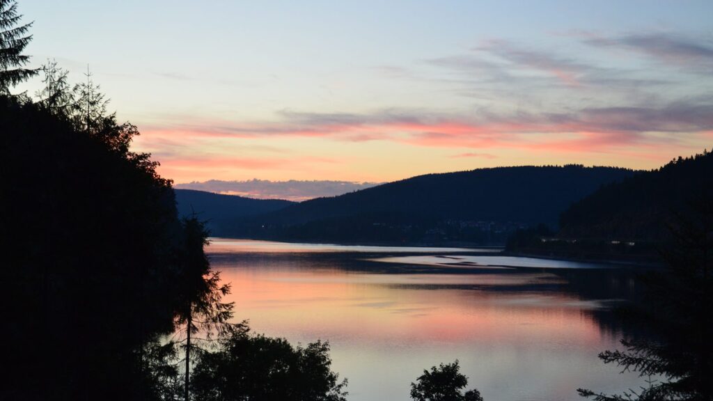 Abendrot über dem Schluchsee mit bewaldeten Schwarzwaldhöhen und dem Ort am Ufer