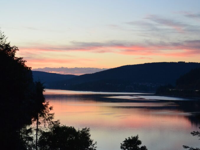 Abendrot über dem Schluchsee mit bewaldeten Schwarzwaldhöhen und dem Ort am Ufer