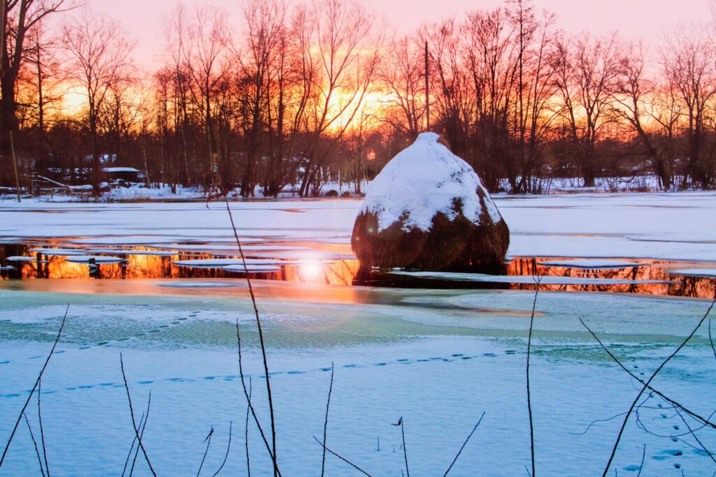 Verschneiter Heuhaufen auf einer gefrorenen Wiese im Spreewald bei Sonnenuntergang