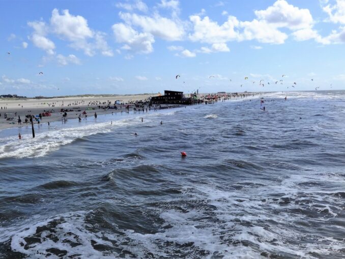 Breiter Sandstrand von St. Peter-Ording mit Pfahlbau, Brandung und vielen Kite-Schirmen
