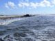 Breiter Sandstrand von St. Peter-Ording mit Pfahlbau, Brandung und vielen Kite-Schirmen