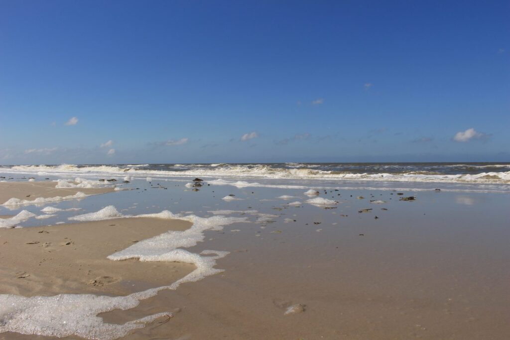 Auslaufende Brandung und Schaum auf dem hellen Sandstrand unter blauem Himmel