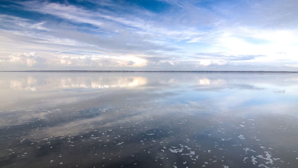 Weite Wasserfläche des Steinhuder Meeres mit Wolkenspiegelung und flachem Uferstreifen am Horizont