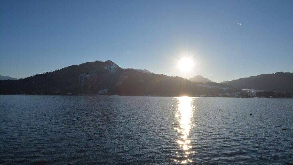 Winterlicher Tegernsee mit tief stehender Sonne und schneebedeckten Berghängen