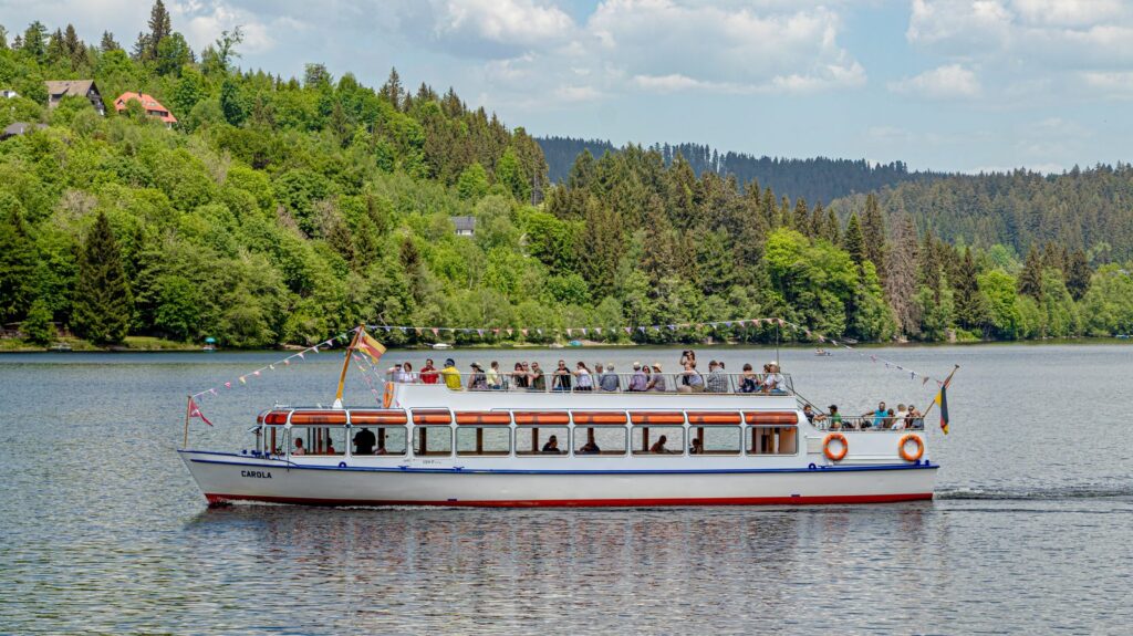 Elektroboot Carola der Titisee-Rundfahrten auf dem See vor bewaldetem Ufer